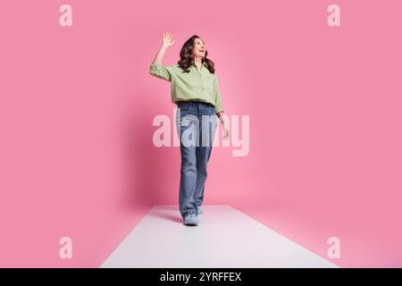 Foto von Senior Lady in formellem Outfit Jeans und Khaki Hemd gehen Podium winkend handfreundliche Grüße isoliert auf rosa Hintergrund Stockfoto