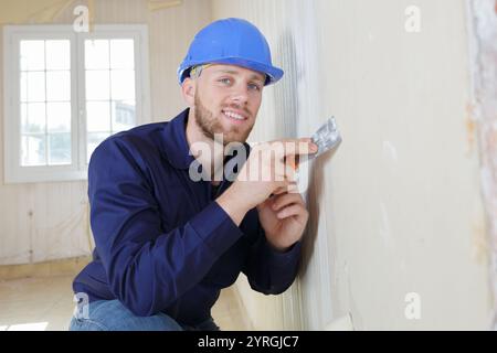 Glücklicher Arbeiter hat den Mörtel an die Wand gestopft Stockfoto