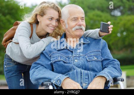 Tochter und Vater sitzen im Rollstuhl und machen Selfie Stockfoto