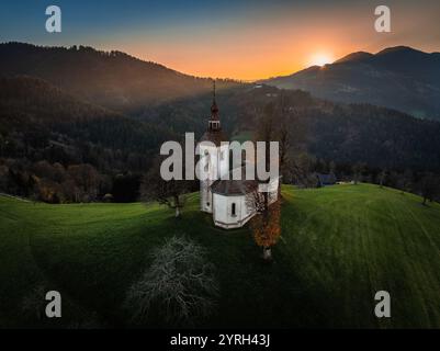 Skofja Loka, Slowenien - Blick aus der Vogelperspektive auf die wunderschöne Kirche Sveti Tomaz (St. Thomas) mit untergehender Sonne im Hintergrund an einem Herbstnachmittag Stockfoto