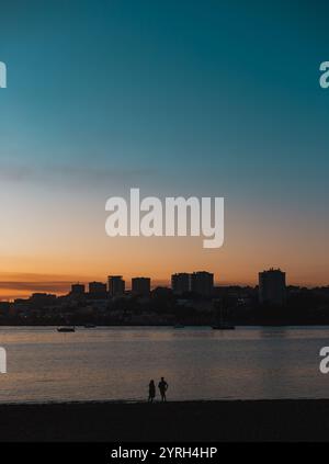 Zwei Personen genießen einen wunderschönen Sonnenuntergang über dem Fluss douro mit dem Stadtbild von Porto im Hintergrund, was eine ruhige und romantische Atmosphäre schafft Stockfoto