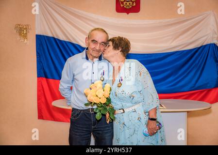 Ein russisches Paar feiert seinen goldenen Hochzeitstag im Standesamt. Das ältere Ehepaar, beide über 70 Jahre alt, trägt stolz Medaillen und teilt eine Stockfoto