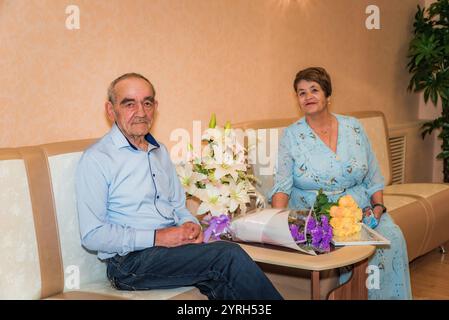 Das russische Paar über 70 feiert seine goldene Hochzeit im Standesamt. Sie sitzen in festlicher Kleidung auf Sofas, lächeln in die Kamera, mit Bouquen Stockfoto