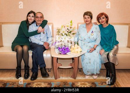 Der 76-jährige Mann und die 71-jährige Frau feiern ihren goldenen Hochzeitstag, sitzen auf einem Sofa im Standesamt, umarmt von ihrer Tochter Stockfoto