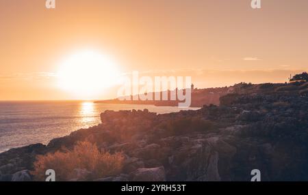 Die untergehende Sonne strahlt ein warmes goldenes Leuchten über die zerklüftete Küste von cascais, portugal, und schafft eine atemberaubende Landschaft voller natürlicher Schönheit und Ruhe Stockfoto