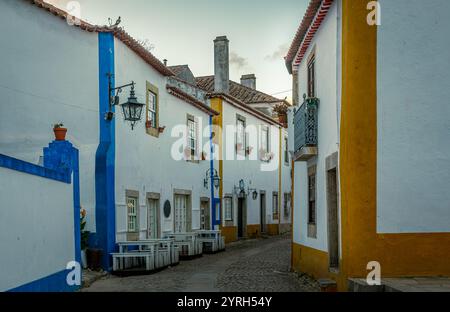 Die kopfsteingepflasterte Straße schlängelt sich durch die historische Stadt Obidos in portugal, mit bezaubernden weißen Häusern, die mit blauen und gelben Akzenten und W verziert sind Stockfoto