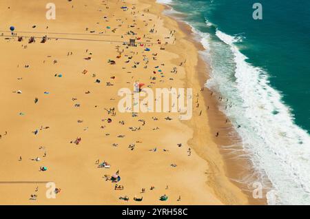 Aus der Vogelperspektive auf den Strand praia de nazare in nazare, portugal, wo Touristen Sonnenbaden und schwimmen und ihren Sommerurlaub genießen Stockfoto