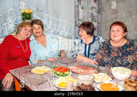 Vier russische Freunde, zwei in ihren 60ern und zwei in ihren 70ern, feiern gemeinsam einen besonderen Anlass. Sie lächeln und posieren für die Kamera beim Abendessen Stockfoto