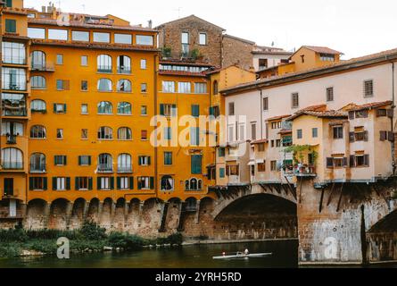 Ruder paddelt den Fluss arno unter der ponte vecchio in florenz, italien, mit farbenfrohen Gebäuden am Flussufer Stockfoto