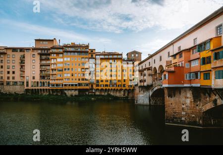 Ponte vecchio reflektiert auf dem Fluss arno unter bewölktem Himmel mit farbenfrohen Gebäuden am Flussufer in florenz, italien Stockfoto