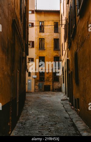 Eine kopfsteingepflasterte Gasse führt zu gelben Gebäuden mit Fenstern und Balkonen in florenz, italien, die die charmante Architektur der Stadt veranschaulichen Stockfoto
