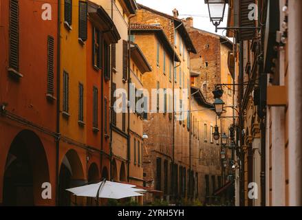 Warmes Licht beleuchtet farbenfrohe Fassaden historischer Gebäude und Straßenlaternen in einer engen Straße von bologna, wodurch eine bezaubernde italienische Atmosphäre entsteht Stockfoto