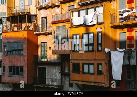 Weiße Wäsche, die auf Balkonen von bunten Gebäuden entlang des onyar-Flusses in girona, katalonien, spanien, zum Trocknen hängt, schafft ein lebendiges und malerisches s Stockfoto