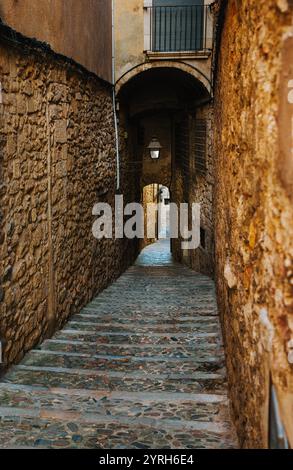 Steintreppen steigen durch einen schmalen, bogenförmigen Durchgang in gironas Altstadt hinauf und zeigen die mittelalterliche Architektur und den zeitlosen Charme der Stadt Stockfoto