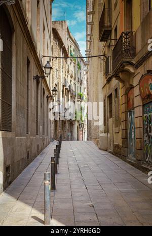 Eine gepflasterte Gasse aus Stein erhebt sich zwischen alten Gebäuden mit Balkonen und Straßenlaternen im gotischen Viertel von barcelona, spanien Stockfoto