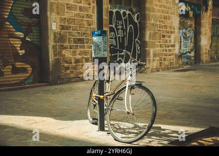 Altes, möglicherweise verlassenes Fahrrad ist an einem Stab mit einem Stadtplan befestigt, der in einer engen Straße von barcelonas gotischem Viertel befestigt ist Stockfoto
