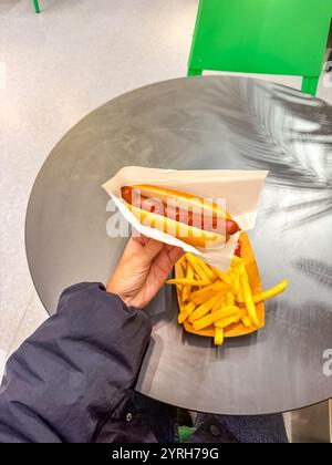 Weibliche Hand, die einen Hot Dog mit Pommes auf einem Teller auf Holztisch hält. Hochwertige Fotos Stockfoto
