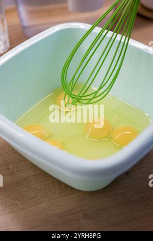 Eier in einer weißen Plastikschale rühren. Koch- oder Backprozess. Stockfoto