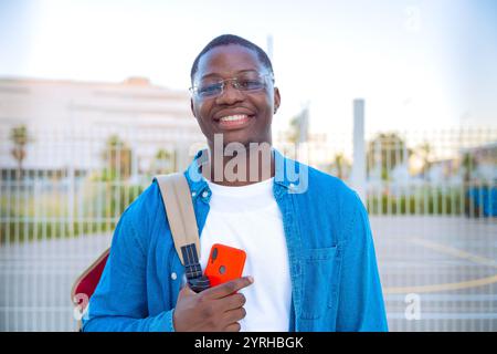 Ein lächelnder junger Mann, der im Freien Smartphone und Notebooks in lässiger Kleidung hält Stockfoto