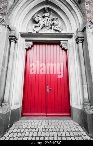 Hellrote Tür im schwarz-weißen Eingangsbereich. Der alte Eingang zu einer Kirche. Stockfoto