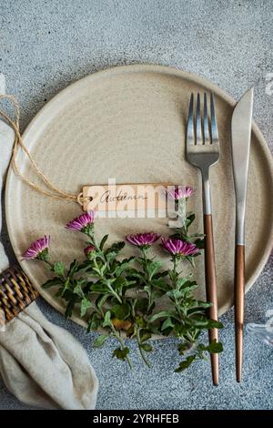 Elegante Tischeinrichtung mit beigefarbenem Teller mit Blumenarrangements, rustikalem Namensschild mit der Aufschrift „Herbst“ und elegantem Besteck, das die Saison darstellt Stockfoto
