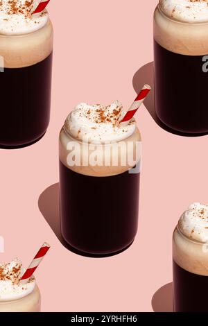 Ein kreatives Arrangement dunkler Kaffeegetränke mit Schlagsahne und gestreuten Gewürzen, serviert in Glasgläsern mit gestreiften Strohhalmen gegen ein Pastell Stockfoto
