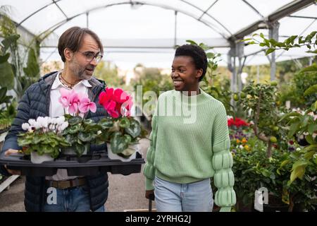 Zwei Personen genießen Einkaufen in einem Gewächshaus voller üppiger Pflanzen und farbenfroher Blumen. Sie teilen einen Moment der Freude, umgeben von einer Vielzahl von Planen Stockfoto