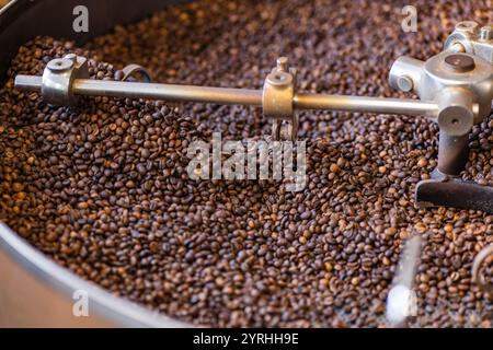 Nahaufnahme frisch gerösteter Kaffeebohnen in einer industriellen Röstmaschine, die ihre satte Farbe und Textur erfasst. Die Maschine verarbeitet große Mengen Stockfoto