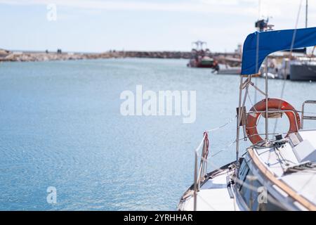 Ein ruhiger Blick auf ein Segelboot, das in einem sonnendurchfluteten Hafen angedockt ist, das Wasser, das sanft unter einem klaren Himmel plätschert, Und Ein lebendiger Rettungsschirm verleiht dem Frieden einen Farbtupfer Stockfoto