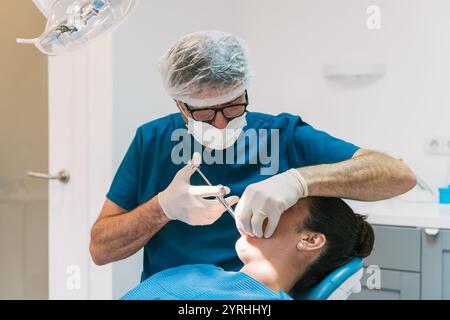 Zahnarzt in blauen Peelings und Maske bereitet sich auf die Narkose an einen Patienten vor. Die Umgebung ist eine moderne Zahnklinik mit einer hellen, sterilen Umgebung Stockfoto