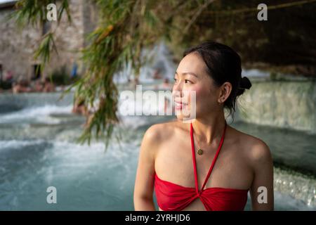 Eine asiatische Frau in rotem Badeanzug entspannt sich in der Terme di Saturnia, Toskana die natürliche Schönheit der Thermalquellen bietet einen ruhigen und ruhigen Rückzugsort Stockfoto