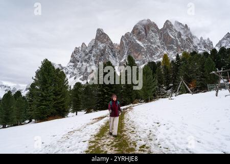 Ein asiatischer Wanderer genießt einen schneebedeckten Pfad in den Dolomiten Italiens, umgeben von den atemberaubenden Gipfeln des Naturparks Puez Geisler, der die Ruhe des Winters zeigt Stockfoto