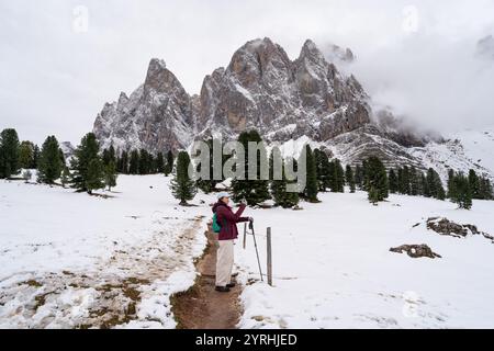 Ein asiatischer Wanderer fängt die atemberaubende Winterlandschaft des Naturparks Puez Geisler in den Dolomiten ein, Italien schneebedeckte Gipfel und üppig grüne Bäume Stockfoto