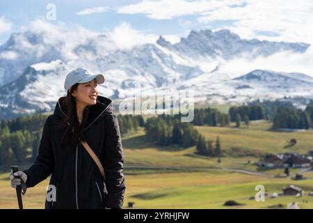 Eine asiatin genießt ein Wanderabenteuer inmitten der atemberaubenden Alpenlandschaft der Seiser Alm in den Dolomiten, Italien, mit saftig grünen Wiesen und Schnee Stockfoto