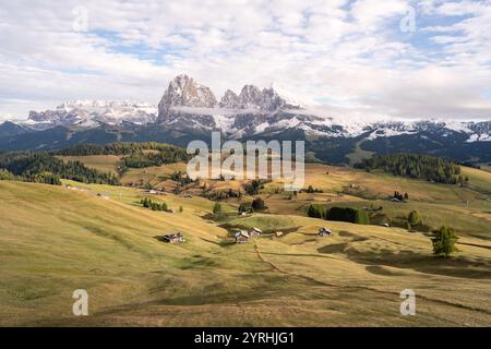 Atemberaubende Landschaft der Seiser Alm in den Dolomiten, Italien weite grüne Wiesen und verstreute Hütten vor majestätischen, schneebedeckten Berggipfeln Stockfoto