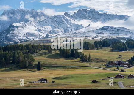 Atemberaubender Blick auf die Seiser Alm in den Dolomiten, Italien schneebedeckte Gipfel umgeben üppige Almwiesen mit rustikalen Holzchalets unter einem Hauch Stockfoto