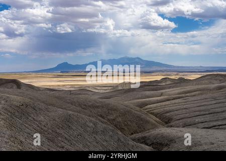 Ein atemberaubender blick auf die sanften Wüstenhügel unter einem dramatischen Himmel in Hanskville, Utah. Die ferne Bergkette fügt Tiefe hinzu und fängt das Wesen der Natur ein Stockfoto