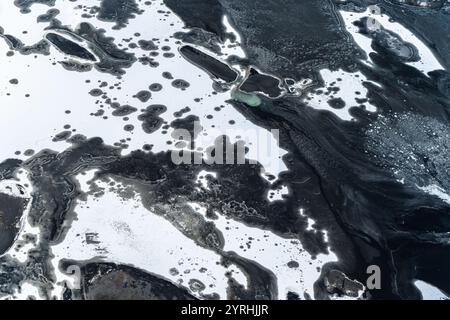 Luftaufnahme, die die atemberaubenden natürlichen Muster von Eis und Felsen an der Südküste Islands und den Kontrast zwischen dunkler vulkanischer Oberfläche und weiß einfängt Stockfoto