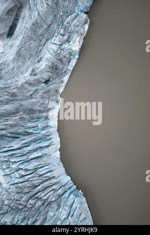 Luftaufnahme mit komplexen Gletschertexturen, die an heiteres braunes Wasser Grenzen, das Bild unterstreicht den starken Kontrast zwischen dem natürlichen Eis Stockfoto