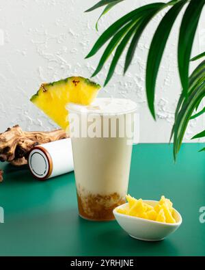 Ein erfrischender tropischer Bubble-Tee mit einer Ananasscheibe, mit leuchtenden grünen Elementen und einer kleinen Schüssel mit gewürfelten Ananasscheiben, die ein s bilden Stockfoto