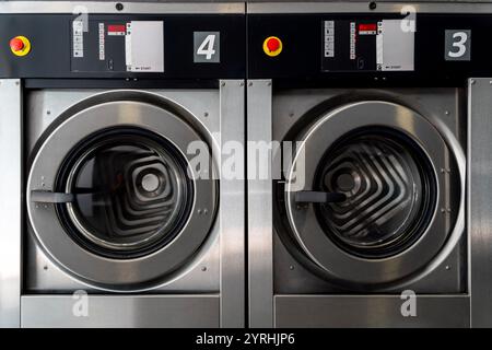 Nahaufnahme von zwei großen industriellen Waschmaschinen in einer modernen Waschanlage mit Edelstahldesigns und digitalen Bedienfeldern. Stockfoto