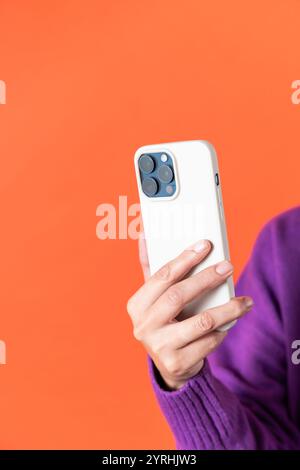 Eine Nahaufnahme einer weiblichen Hand, die ein modernes Smartphone mit drei Kameras vor einem leuchtenden orangefarbenen Hintergrund hält Stockfoto