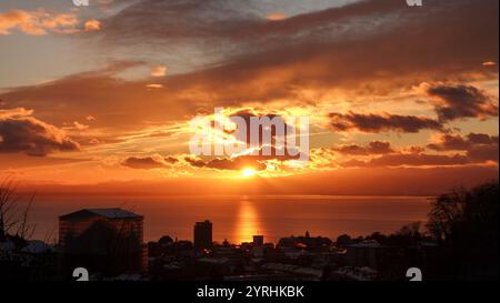 Ein atemberaubender Sonnenuntergang aus Lausanne, Schweiz die Sonne geht spektakulär hinter den Wolken unter und lässt das Wasser und die Stadtlandschaft in lebendigen Tönen erscheinen Stockfoto