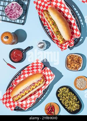 Köstliche Hot Dogs serviert mit Senf, umgeben von Belägen und Gewürzen, schaffen eine optisch appetitliche Einrichtung auf einer hellblauen Oberfläche Stockfoto