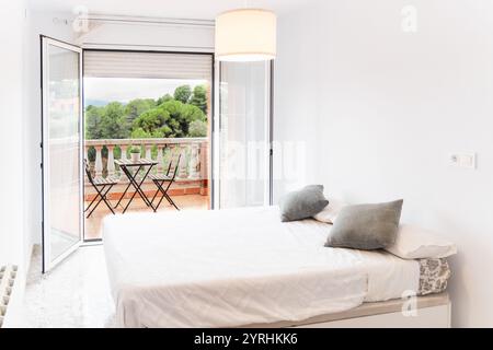 Modernes Schlafzimmer mit komfortablem Bett und elegantem Dekor offene Türen führen zu einer Terrasse mit malerischem Blick auf das üppige Grün und schaffen eine ruhige Atmosphäre Stockfoto