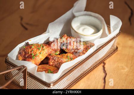 Ein Korb mit knusprigen Hähnchenflügeln, gewürzt und garniert mit Schnittlauchschnitzel, serviert mit einer cremigen Dippsauce, perfekt für einen herzhaften Snack oder Appetit Stockfoto