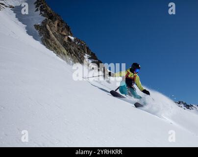 Eine Skifahrerin in lebendiger Ausrüstung schneidet sich an einem sonnigen Tag vor einem klaren blauen Himmel durch frischen Powder, fährt bergab und zeigt Geschick und Spannung in einem W Stockfoto