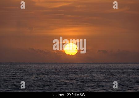 Fesselnder Blick auf einen goldenen Sonnenuntergang über einem ruhigen Meer, der warme Töne über den Himmel wirft und auf den sanften Wellen Ein ruhiges Bild reflektiert Stockfoto