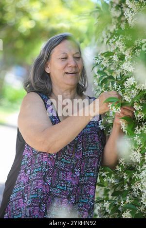 Porträt einer älteren südamerikanischen gebürtigen Frau in ihrem Garten bei ihrem Haus am sonnigen Sommertag, die sich um Blumenpflanzen kümmert Stockfoto