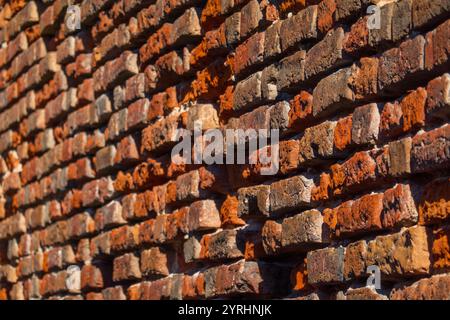 Detaillierte Ansicht der robusten roten Ziegelwand mit einzigartiger Textur und warmen Tönen. Natürliches Licht hebt die komplizierte Oberfläche hervor und vermittelt einen Eindruck von Tiefe und Charakter im architektonischen Design. Stockfoto